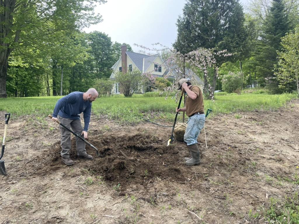 Two crew members digging out a new bed, spring blossoms behind them